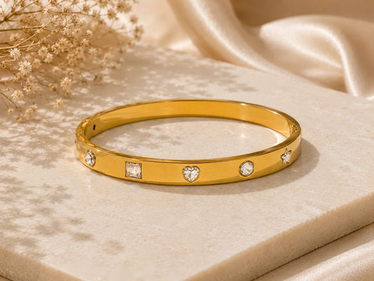 Gold-tone kada bangle with heart centerpiece and gem-detail border, top view