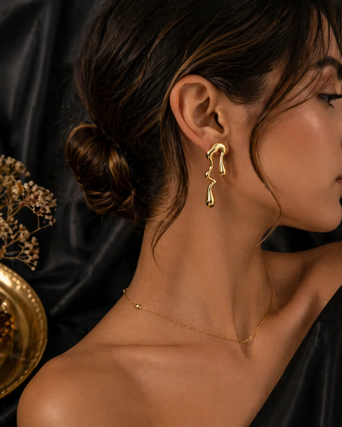 Gold-tone wavy drop earrings with hook backs, worn on model ear