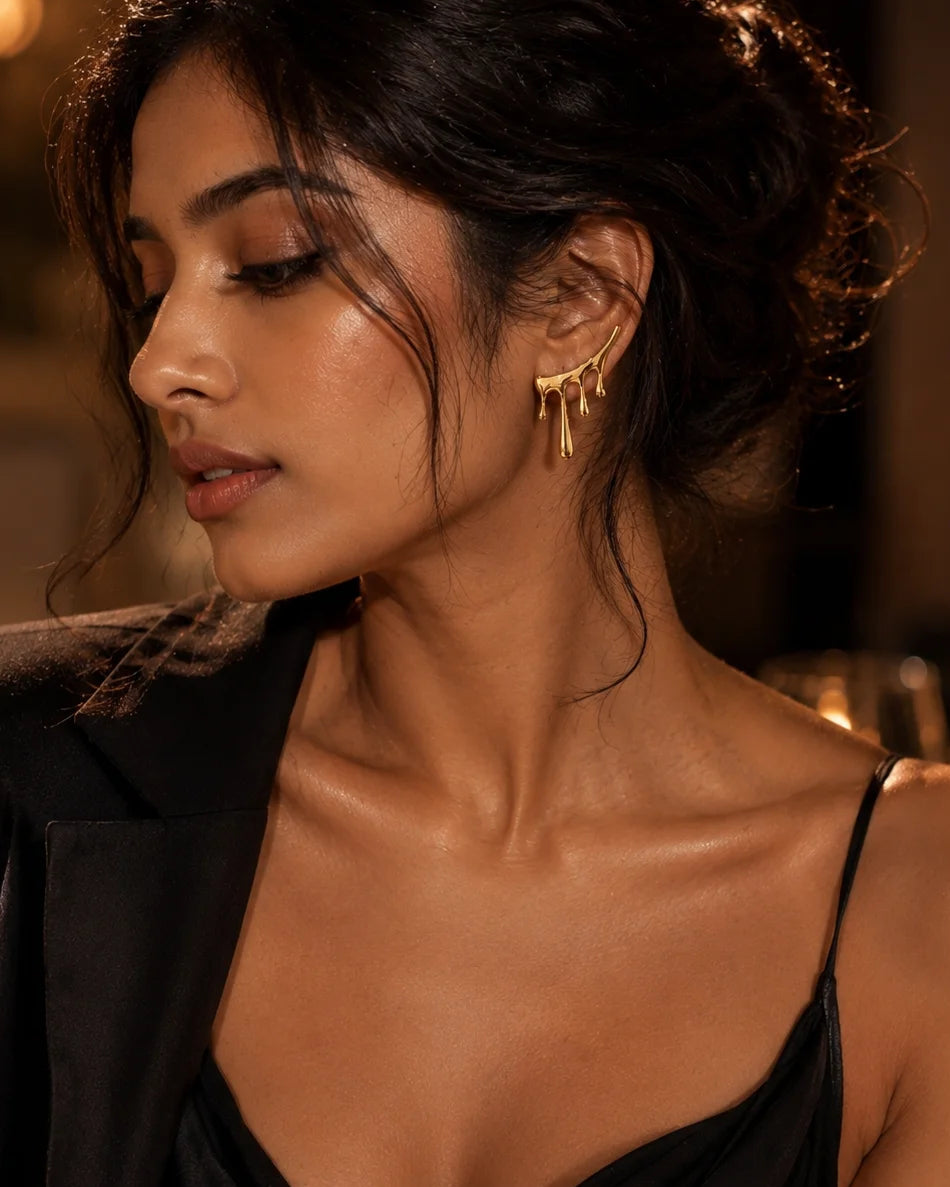 Gold statement earrings with dangling drip charms, worn on model’s ear.