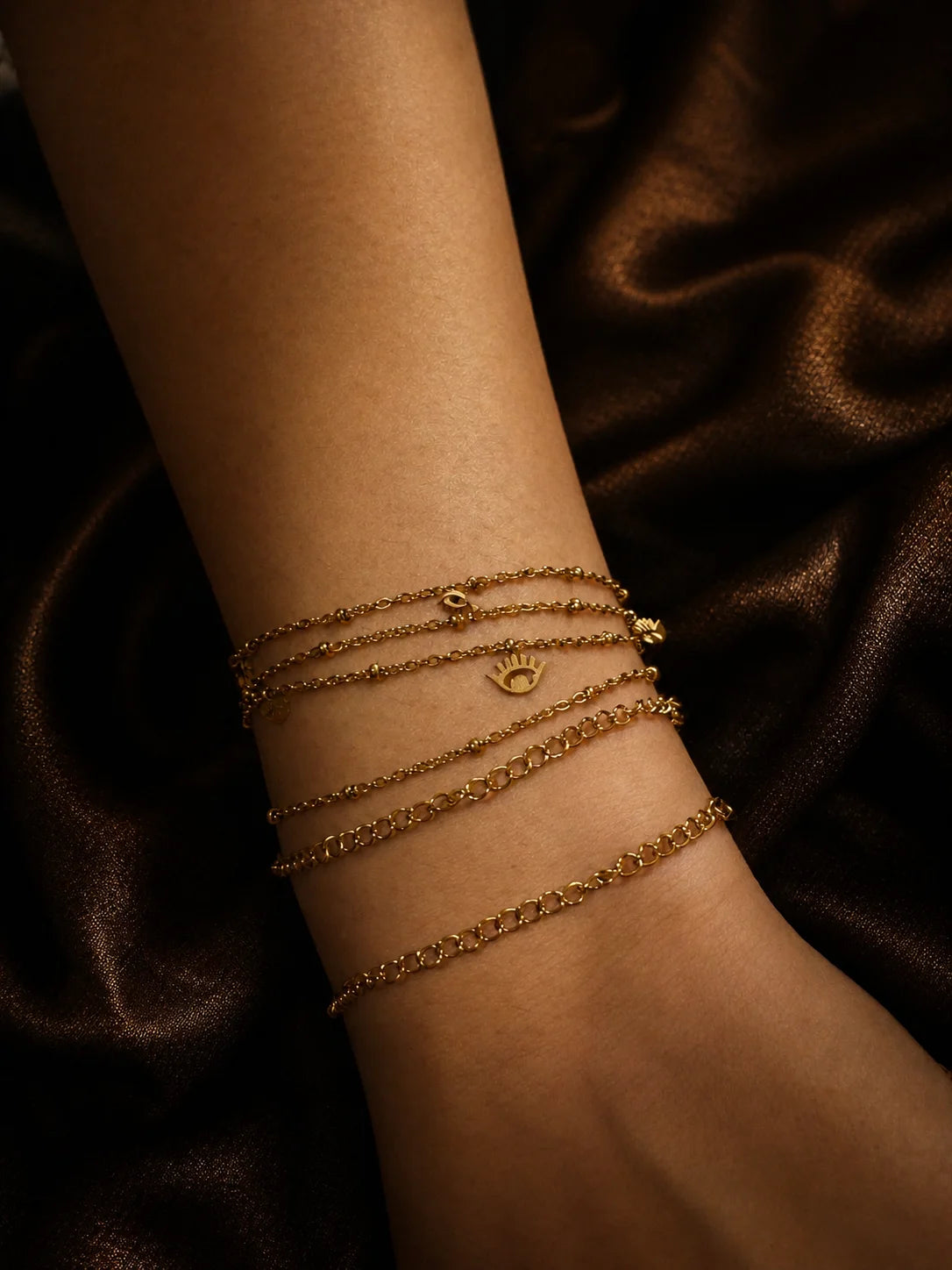 Gold-plated stacked chain bracelets with small charm pendants on wrist