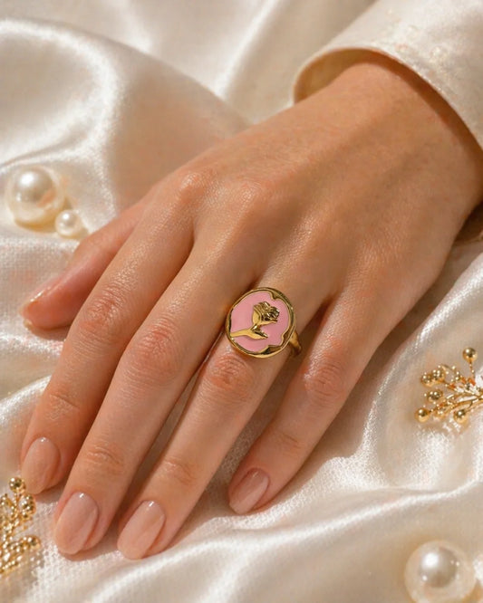 Gold-tone ring on hand with oval pink enamel face and raised hand/rose design