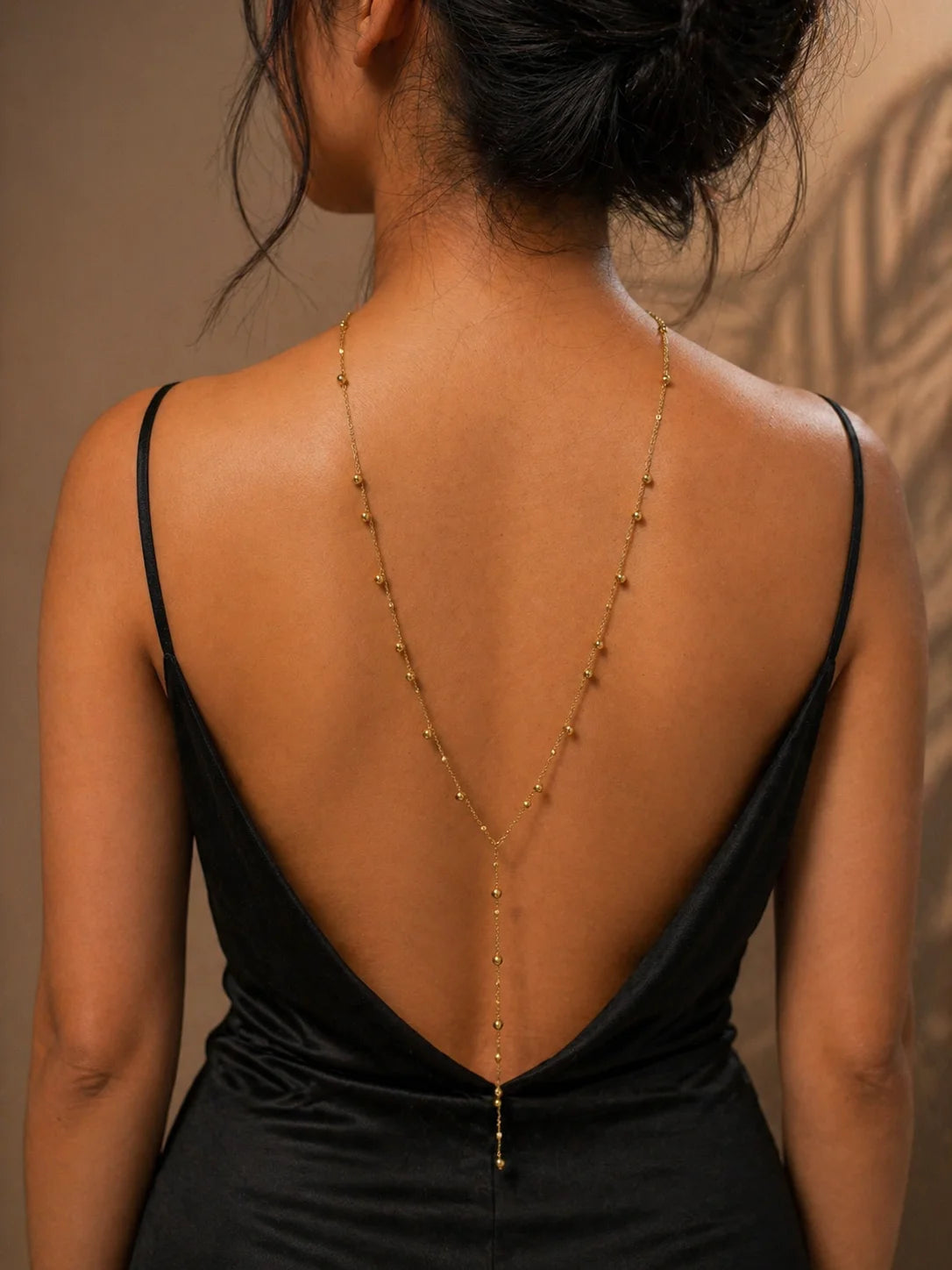 Backdrop chain necklace with gold bead links down open back on black dress